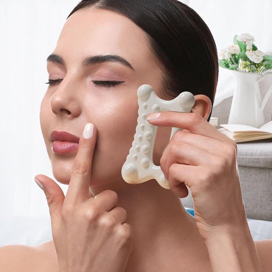 femme se masse délicatement la joue gua sha blanc