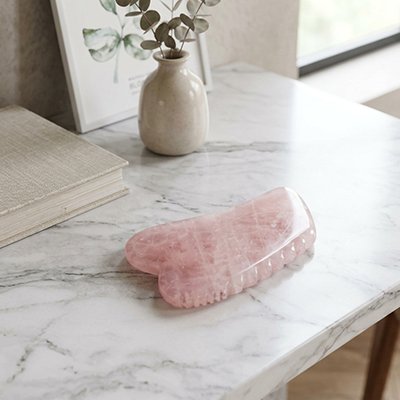 Gua sha rose clair posé sur meuble marbre gris